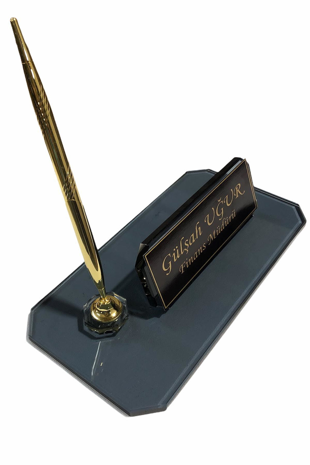 Angled view of a dark glass desk nameplate with a personalized gold-bordered plate and one gold-tone pen