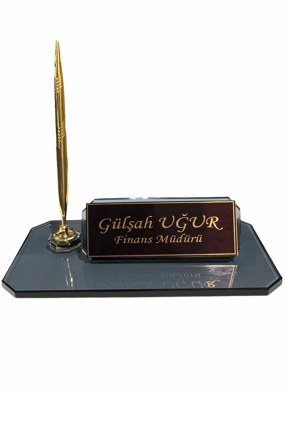 Dark glass desk nameplate with a personalized gold-bordered plate and one gold-tone pen on a beveled rectangular base