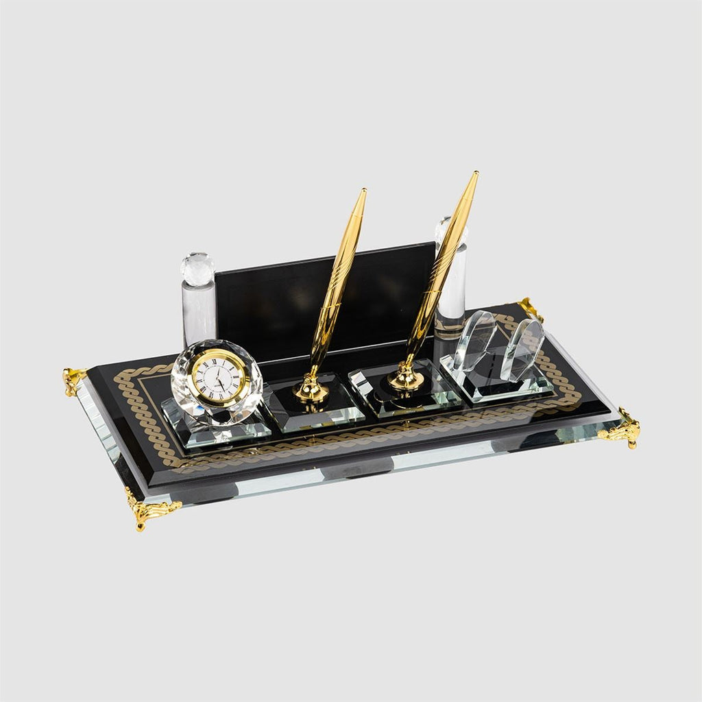 Black glass desk nameplate set with two gold-tone pens, a clock and a clear card holder, viewed at an angle