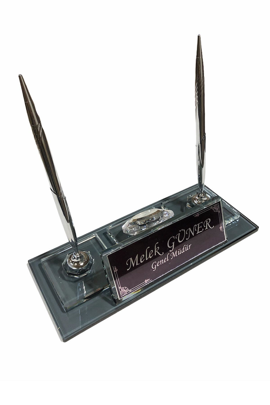 Dark glass desk nameplate with an engraved panel and two silver-colored pens, viewed at an angle.