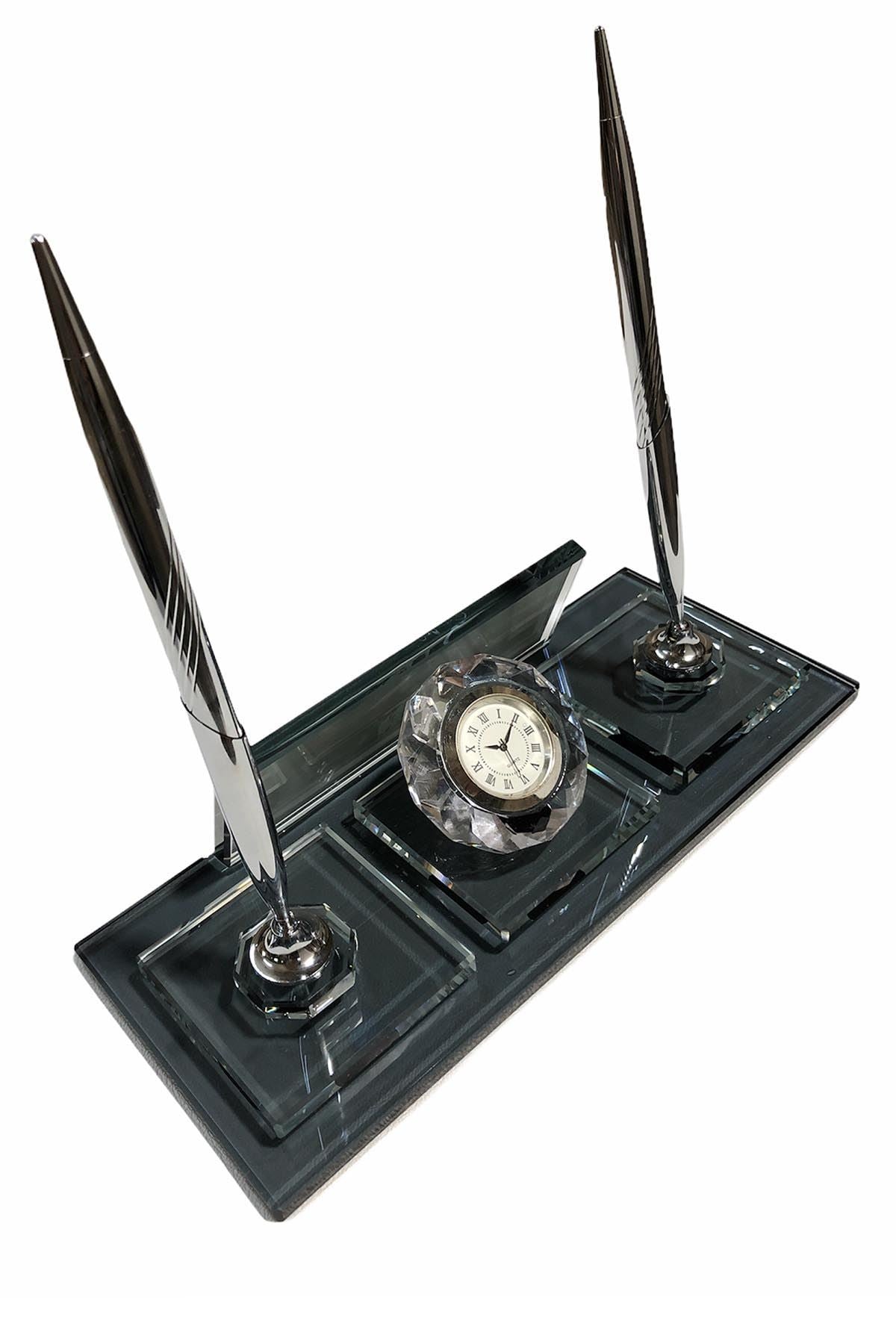 Dark glass desk nameplate with two silver-colored pens and a central round clock, viewed from the reverse side.