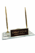 Clear desk nameplate with a dark engraved panel and two gold-colored pens on a transparent rectangular base.